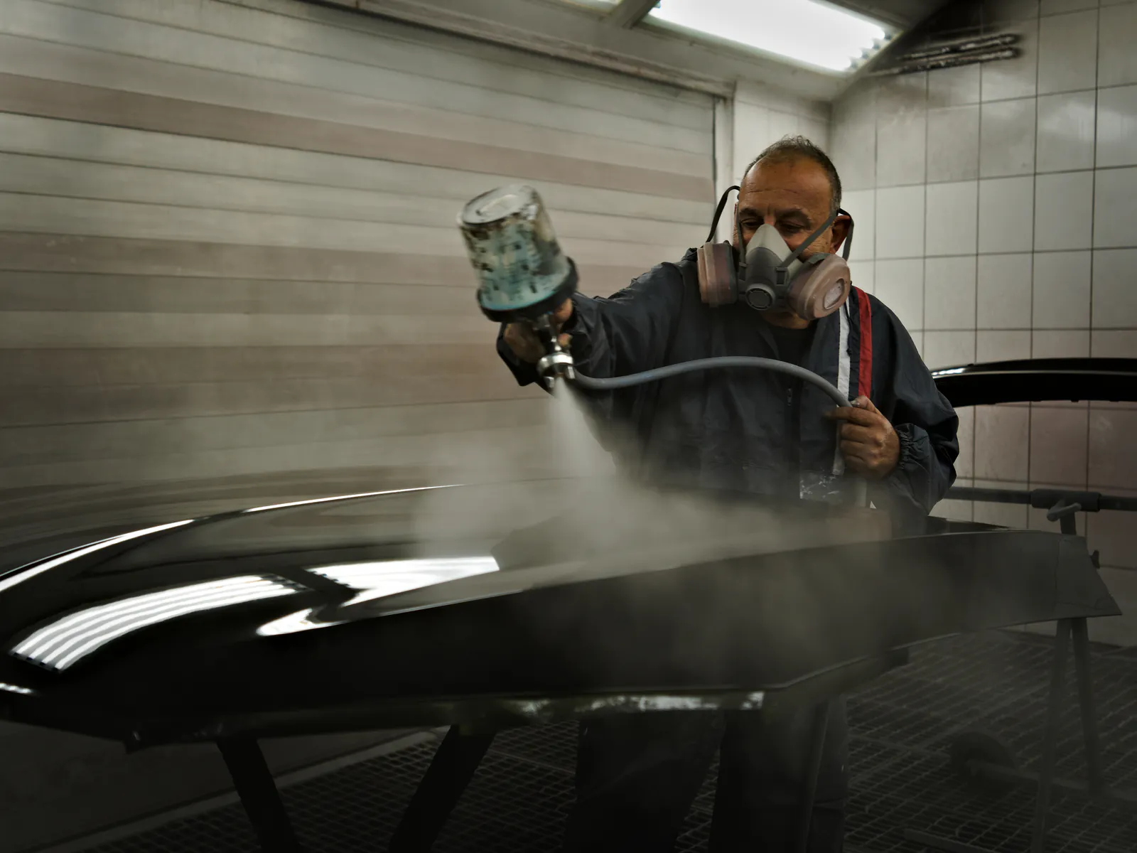 Lackierer sprüht mit der Spritzpistole Farblack in der Lackierkabine